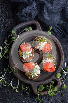 Delicious canape with salmon, cottage cheese, olive with micro greens on a dark background. Cold appetizer.