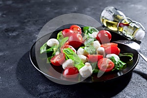 Delicious caprese salad with ripe cherry tomatoes and mini mozzarella cheese balls with fresh basil leaves on black