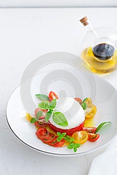 Delicious caprese salad with ripe cherry tomatoes and mozzarella cheese with fresh basil leaves and olive oil. Italian