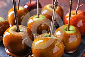 Delicious caramel apples with tree branches on slate plate