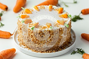 Delicious carrot cake decorated with mastic sweet carrots. Homemade carrot cake with yellow crumbs in the white plate