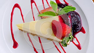 Delicious cheesecake with fresh strawberries and mint is served on a white plate in a cafe