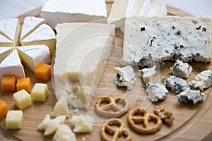 Delicious cheeses: camembert, blue cheese, brie, parmesan, mimolette and edam with pretzels and walnuts on round wooden board.