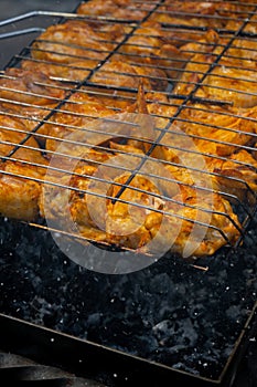 Delicious chicken frying on barbecue grill grate outdoor. Seasoning falling on fresh grilled chicken wings. Summer party