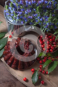 Delicious chocolate cake with berry of sweet cherry, vintage kettle and bouquet of blue flowers on dark wooden background