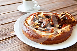 Delicious chocolate cake in white plate and one piece of chocolate cake with cup of coffee on wooden table background