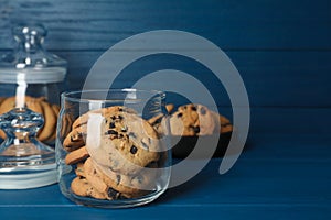 Delicious chocolate chip cookies in glass jar on blue wooden table, space for text