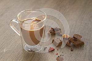 Delicious chocolate milk with pieces of chocola on wooden table.