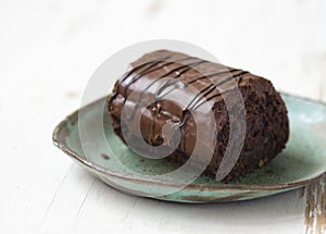 Delicious chocolate roll cake in ceramic plate on white wooden background