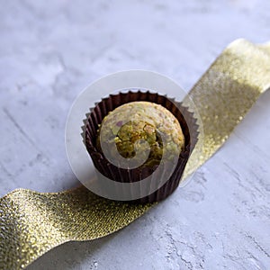 Delicious chocolate truffle in brown candy wrapper stands on a golden ribbon on a gray concrete background.