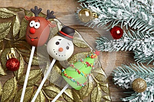 Delicious Christmas themed cake pops and fir tree branches with balls on wooden table, flat lay