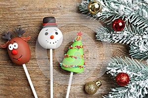 Delicious Christmas themed cake pops and fir tree branches with balls on wooden table, flat lay