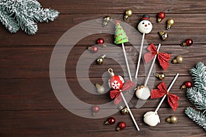 Delicious Christmas themed cake pops with fir tree branches and balls on wooden table, flat lay. Space for text