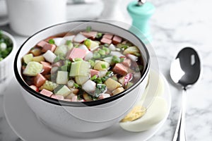 Delicious cold okroshka with kvass served on marble table, closeup. Traditional Russian summer soup