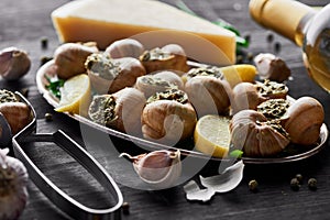 Delicious cooked escargots with lemon slices on black wooden table with spices and white wine.