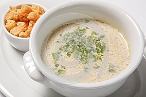 Delicious creamy soup with croutons and greens on white dish