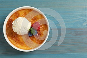 Delicious creme brulee with scoop of ice cream, fresh berries and mint on light blue wooden table, top view. Space for text