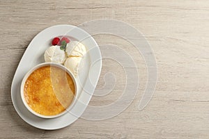 Delicious creme brulee with scoops of ice cream, fresh raspberries and mint on light wooden table, top view. Space for text
