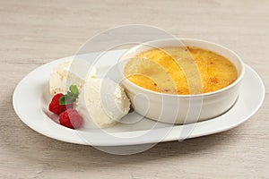 Delicious creme brulee served with scoops of ice cream, fresh raspberries and mint on light wooden table