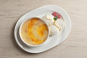 Delicious creme brulee served with scoops of ice cream, fresh raspberries and mint on light wooden table, top view