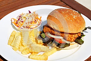 A delicious crispy fish burger with cheese, lettuce, and mayonnaise with french fries and salad onside.