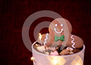 Delicious cup of hot chocolate inside a white cup with a gingerbread man cookie dipped in it with chocolates on top sprinkled with