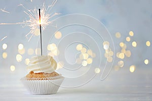 Delicious cupcake with sparkler on white table against blurred lights