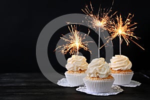 Delicious cupcakes with sparklers on wooden table against dark background