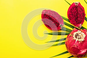 Delicious cut and whole red pitahaya fruits with palm leaf on yellow background, flat lay. Space for text