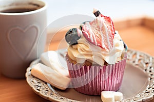 Delicious dessert and coffee in a heart dessin mug on a tray. Creamy muffin cupcake decorated with strawberry and sweets - desatur