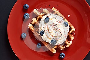 Delicious dessert. Top view of a traditional Belgian Waffle with cream and fresh blueberry on red plate