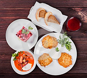 Delicious dinner table with potato pancakes, traditional beetroot soup - borscht with beef, beet salad Vinaigrette.