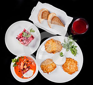 Delicious dinner table with potato pancakes, traditional beetroot soup - borscht with beef, beet salad Vinaigrette