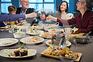 Delicious dishes on restaurant table people raising wine glasses on background
