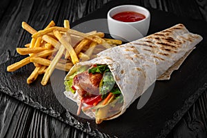A delicious doner donair kebab wrap with meat, lettuce, tomato, red onion and sauce with french fries photo
