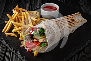 A delicious doner donair kebab wrap with meat, lettuce, tomato, red onion and sauce with french fries photo