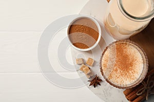 Delicious eggnog with anise and cinnamon on white wooden table, flat lay. Space for text