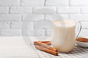 Delicious eggnog with cinnamon on wooden table, space for text