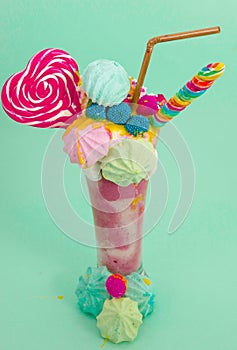 Delicious extreme milkshake of strawberry with dragees and a blackberry candy over a milk foam with a plastic straw and