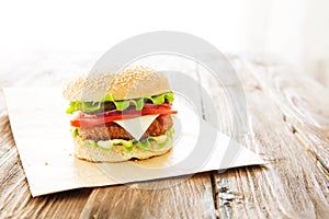 Delicious fast food. Cheese burger with grilled meat, cheese, tomato, on craft paper on wooden surface. Fast food