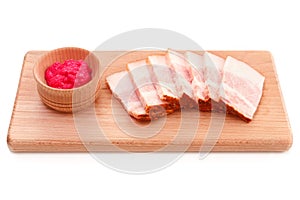 Delicious fat pork jowl bacon with horseradish sauce on wooden plate