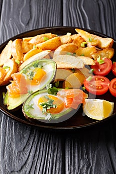 Delicious food: Baked avocado stuffed with eggs and salmon, fresh tomatoes and potato close-up. vertical