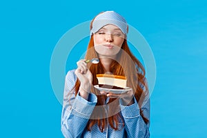 Delicious food, lifestyle and people concept. Delighted and happy cute redhead female in pyjama and sleep mask, close