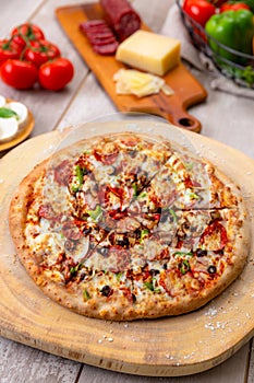 Delicious fresh baked supreme vegetable and meat pizza on wooden board with italian food ingredients, vertical