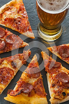 Delicious fresh cooked slices of pepperoni pizza on slate and glass of beer