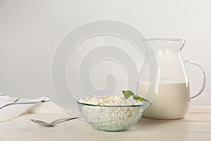 Delicious fresh cottage cheese with basil and milk on white wooden table. Space for text