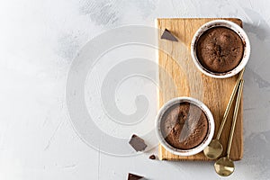 Delicious fresh fondant with hot chocolate centre in ceramic molds on wooden board on white background. Lava cake recipe, menu.