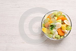 Delicious fresh fruit salad in bowl on white wooden table, top view. Space for text