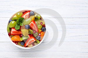 Delicious fresh fruit salad in bowl on white wooden table, top view. Space for text