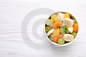 Delicious fresh fruit salad in bowl on white wooden table, top view. Space for text